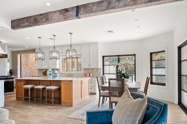 kitchen with a spacious island, white cabinets, light wood-type flooring, and stainless steel gas range oven