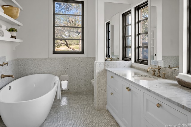 bathroom with a bathing tub, tile walls, toilet, vanity, and tile patterned floors