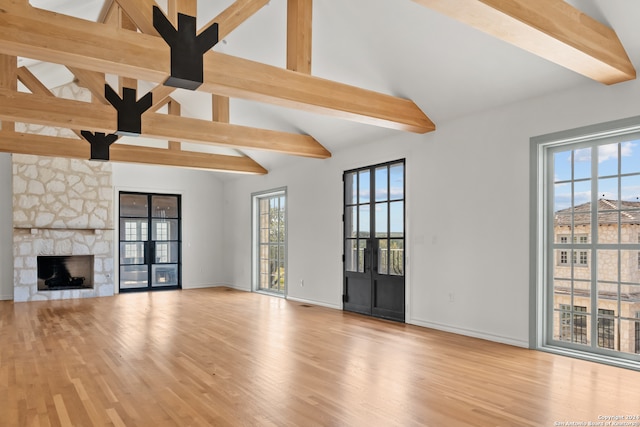 unfurnished living room featuring beamed ceiling, a stone fireplace, light hardwood / wood-style floors, and plenty of natural light