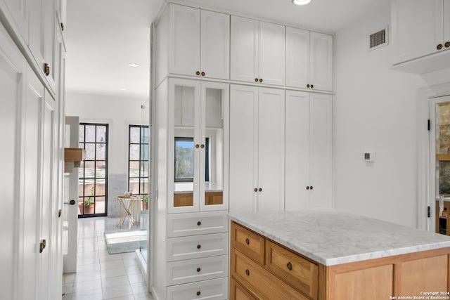 kitchen featuring light tile patterned floors, white cabinetry, light stone countertops, light brown cabinetry, and a center island