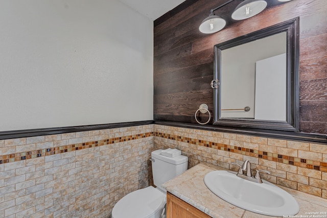 bathroom with vanity, toilet, and tile walls