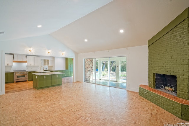 kitchen with white cabinets, high end stove, a center island with sink, a brick fireplace, and sink