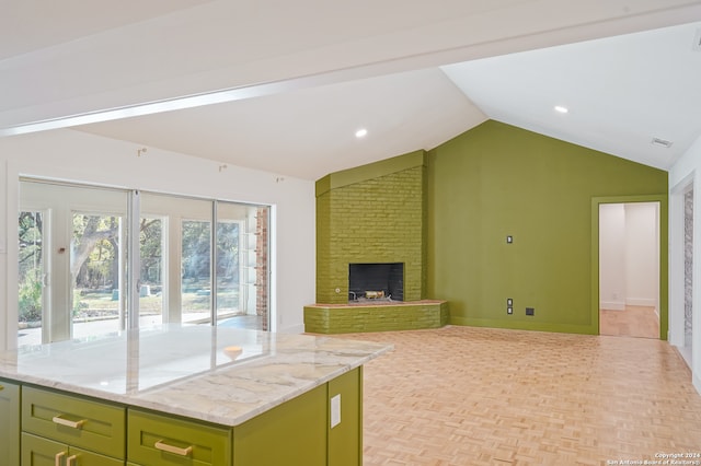 kitchen with light stone countertops, green cabinets, lofted ceiling, and a brick fireplace