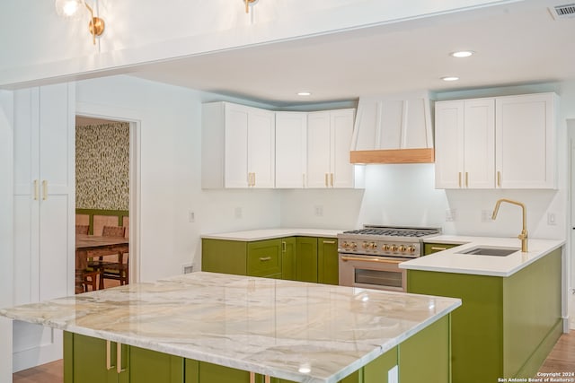 kitchen with sink, green cabinets, high end range, white cabinetry, and custom exhaust hood