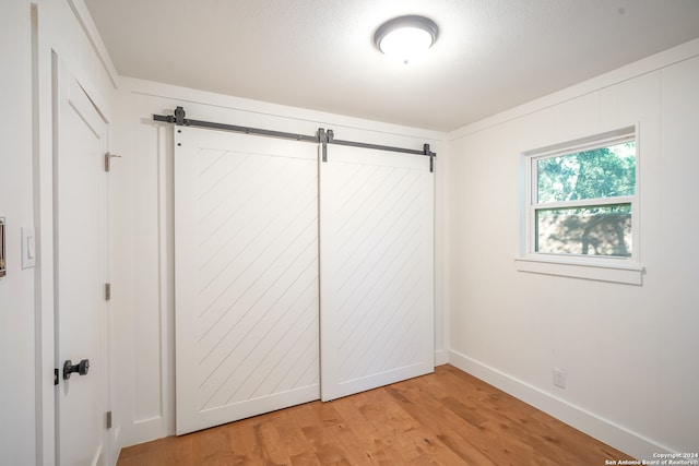 unfurnished bedroom with a barn door and light hardwood / wood-style floors