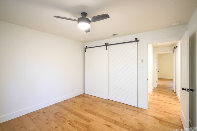 unfurnished bedroom with a closet, ceiling fan, light hardwood / wood-style flooring, and a barn door