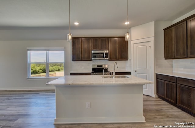 kitchen featuring sink, a kitchen island with sink, light stone counters, and stainless steel appliances