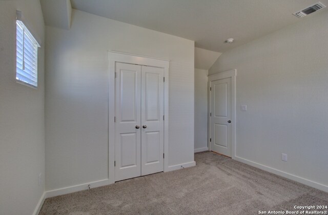 unfurnished bedroom with vaulted ceiling, light carpet, and a closet