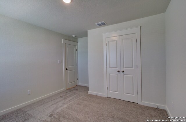 unfurnished bedroom with a textured ceiling, light colored carpet, and a closet