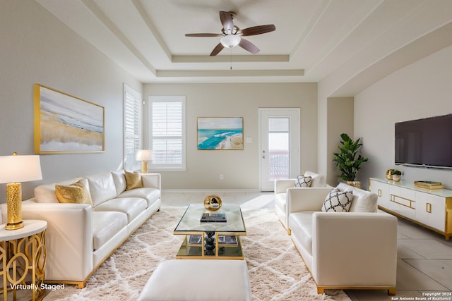 tiled living room with ceiling fan and a raised ceiling