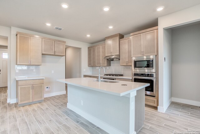 kitchen featuring light brown cabinetry, a kitchen island with sink, light wood-type flooring, and appliances with stainless steel finishes