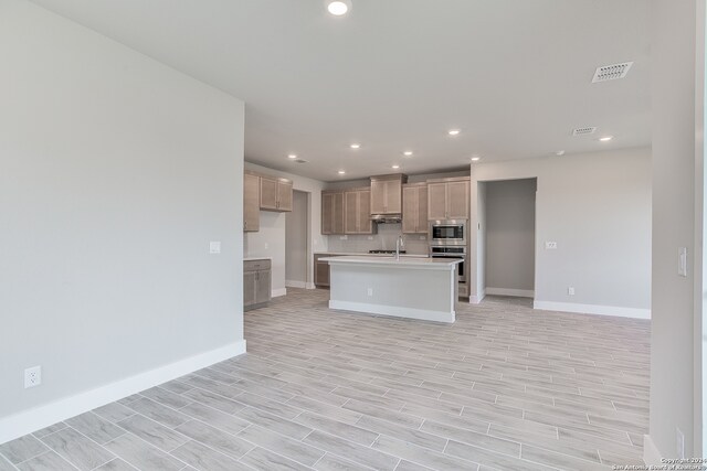 kitchen featuring a center island with sink, light hardwood / wood-style flooring, sink, wall chimney range hood, and appliances with stainless steel finishes