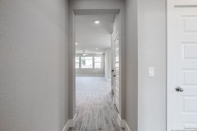 corridor with light wood-type flooring and a textured ceiling