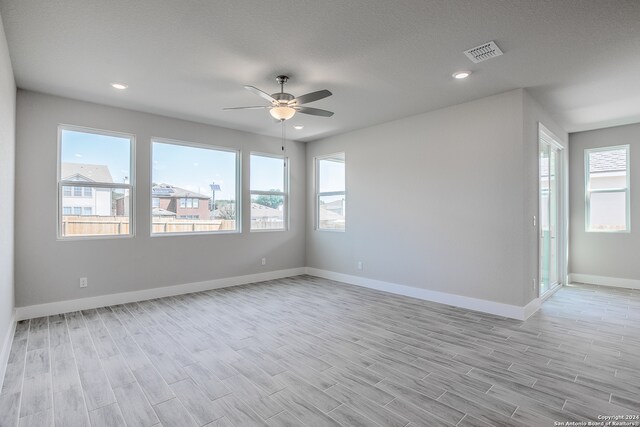 empty room featuring light hardwood / wood-style floors, ceiling fan, plenty of natural light, and a textured ceiling