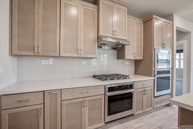 kitchen with light brown cabinetry, backsplash, appliances with stainless steel finishes, and light hardwood / wood-style flooring