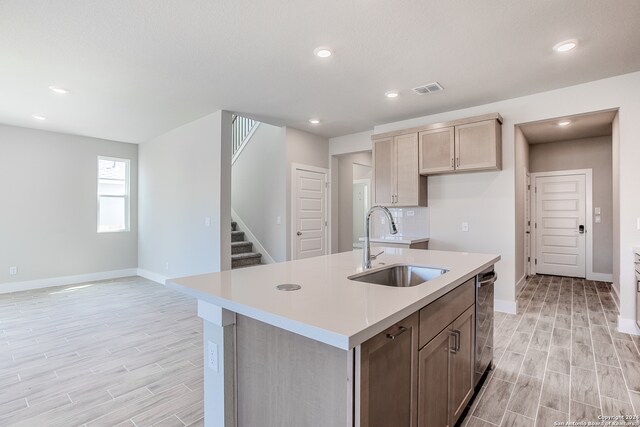 kitchen featuring a kitchen island with sink, stainless steel dishwasher, light hardwood / wood-style flooring, and sink