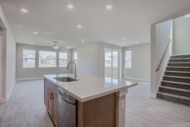 kitchen with stainless steel dishwasher, light hardwood / wood-style floors, sink, and an island with sink