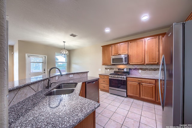 kitchen featuring an island with sink, an inviting chandelier, stainless steel appliances, sink, and decorative light fixtures