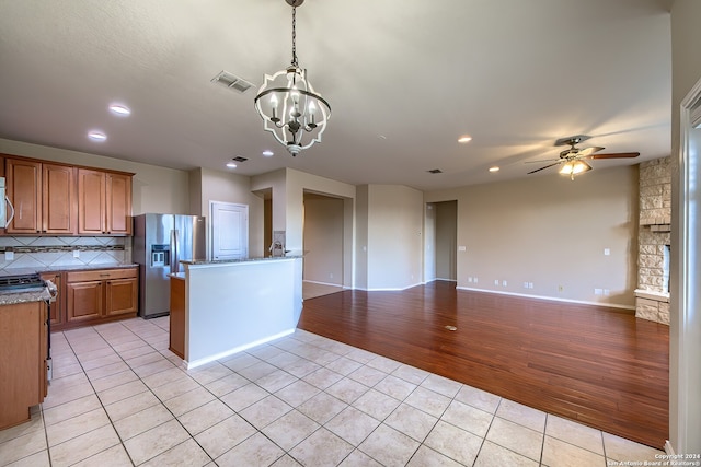 kitchen with tasteful backsplash, appliances with stainless steel finishes, light wood-type flooring, ceiling fan with notable chandelier, and hanging light fixtures