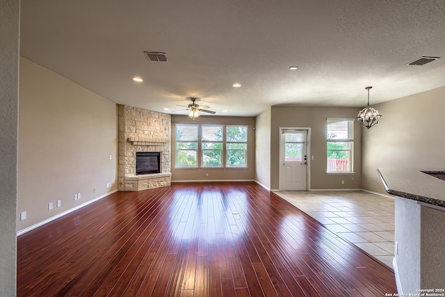 unfurnished living room featuring hardwood / wood-style flooring, a textured ceiling, ceiling fan with notable chandelier, and a stone fireplace