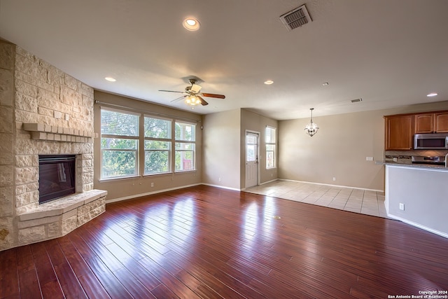 unfurnished living room with ceiling fan with notable chandelier, wood-type flooring, and a fireplace