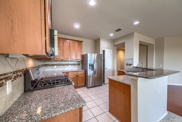 kitchen with light hardwood / wood-style flooring, kitchen peninsula, stainless steel appliances, dark stone countertops, and sink