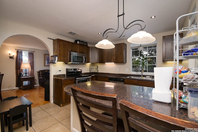 kitchen with sink, stainless steel appliances, dark brown cabinetry, decorative light fixtures, and light hardwood / wood-style flooring