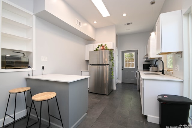 kitchen featuring sink, a kitchen bar, kitchen peninsula, stainless steel fridge, and white cabinetry