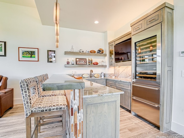 bar featuring light stone counters, decorative light fixtures, beverage cooler, and light hardwood / wood-style flooring