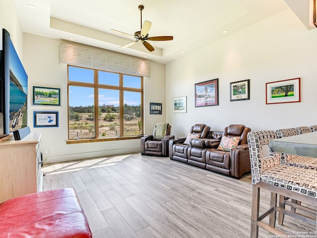 living room with a raised ceiling, light wood-type flooring, and ceiling fan