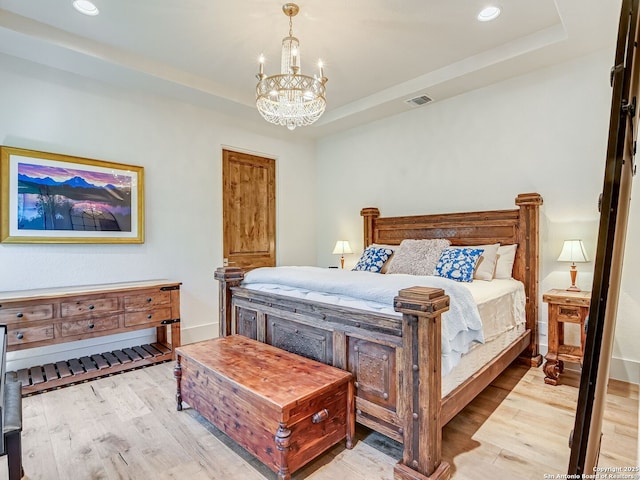 bedroom with a raised ceiling, an inviting chandelier, and light hardwood / wood-style floors