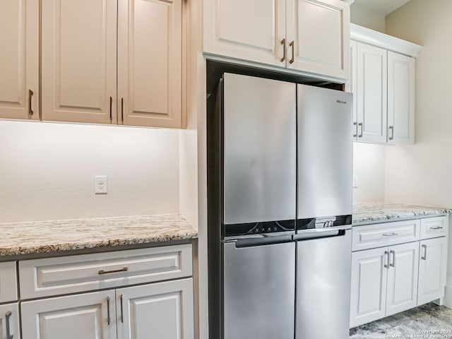 kitchen featuring white cabinets, stainless steel fridge, and light stone countertops