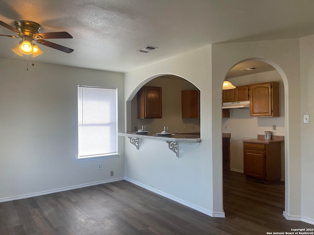 kitchen featuring dark wood-type flooring, ceiling fan, a textured ceiling, and a breakfast bar