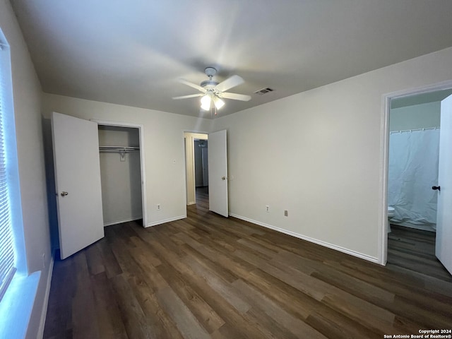 unfurnished bedroom featuring a closet, ensuite bathroom, dark wood-type flooring, and ceiling fan