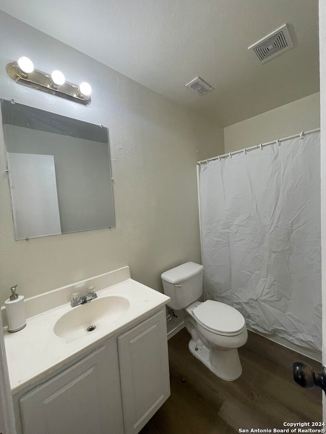 bathroom featuring a textured ceiling, hardwood / wood-style floors, toilet, walk in shower, and vanity