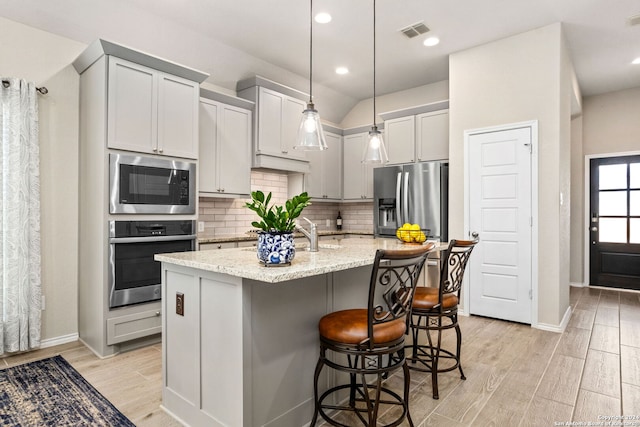 kitchen with a breakfast bar area, an island with sink, pendant lighting, light wood-type flooring, and appliances with stainless steel finishes