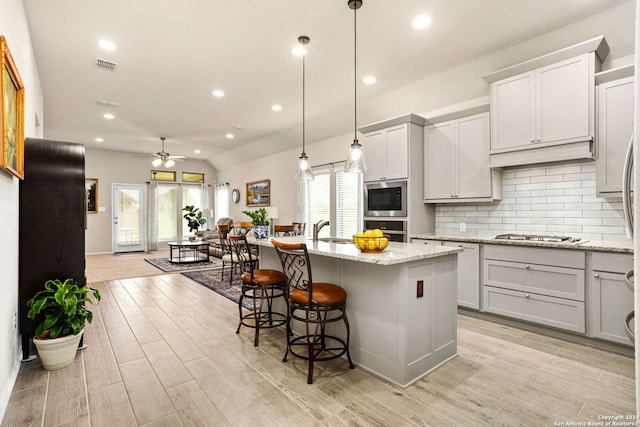 kitchen with a center island with sink, light wood-type flooring, appliances with stainless steel finishes, light stone counters, and ceiling fan