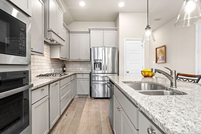 kitchen featuring hanging light fixtures, light stone counters, appliances with stainless steel finishes, light wood-type flooring, and sink