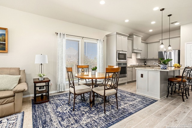 kitchen with a kitchen breakfast bar, an island with sink, hanging light fixtures, light stone countertops, and appliances with stainless steel finishes