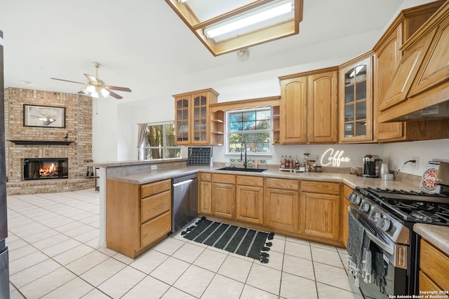 kitchen featuring sink, light tile patterned floors, a fireplace, appliances with stainless steel finishes, and kitchen peninsula