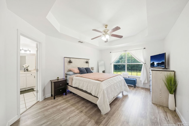 bedroom with ensuite bathroom, light hardwood / wood-style floors, ceiling fan, and a tray ceiling