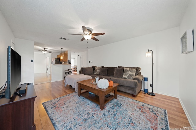 living room featuring ceiling fan, a textured ceiling, and light wood-type flooring