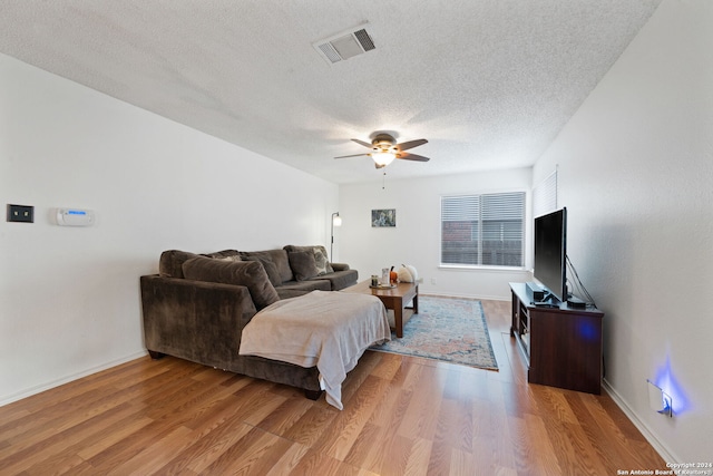 living room with a textured ceiling, light wood-type flooring, and ceiling fan