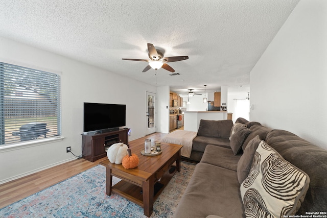 living room with light hardwood / wood-style floors, a textured ceiling, and ceiling fan