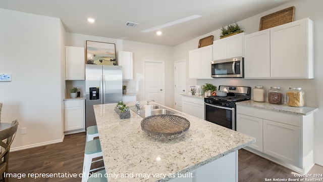 kitchen featuring dark wood-type flooring, appliances with stainless steel finishes, white cabinets, and an island with sink