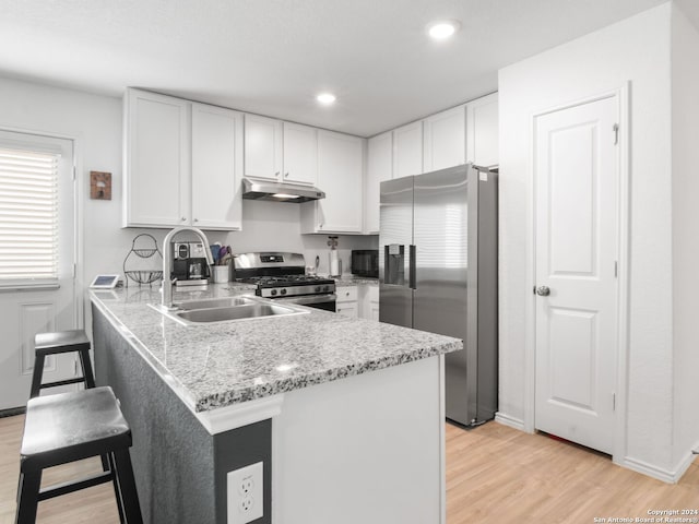 kitchen with kitchen peninsula, stainless steel appliances, light wood-type flooring, white cabinets, and light stone counters