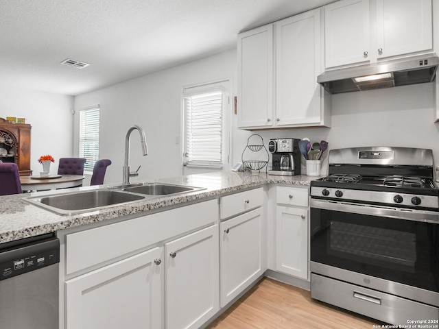 kitchen featuring sink, light stone countertops, white cabinets, appliances with stainless steel finishes, and light hardwood / wood-style floors