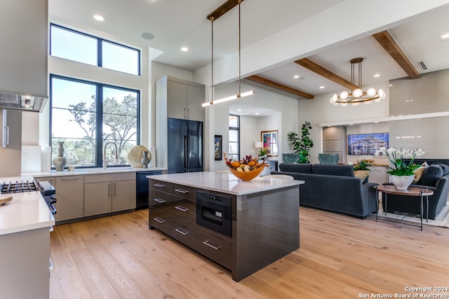 kitchen with beam ceiling, a kitchen island, black appliances, light hardwood / wood-style floors, and decorative light fixtures