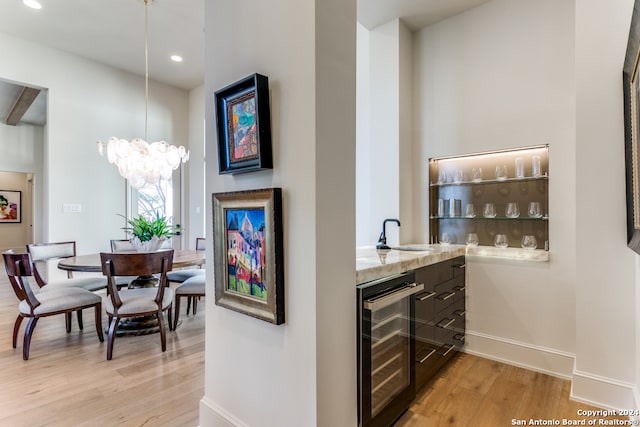 bar with wine cooler, a notable chandelier, sink, and light hardwood / wood-style floors