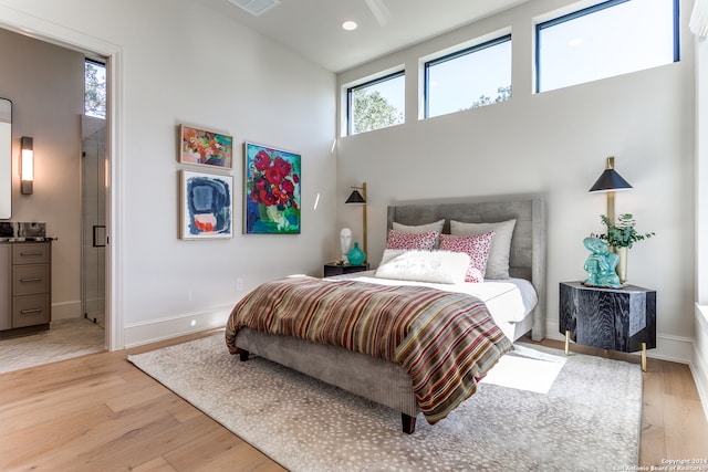 bedroom with light hardwood / wood-style floors, connected bathroom, and a towering ceiling